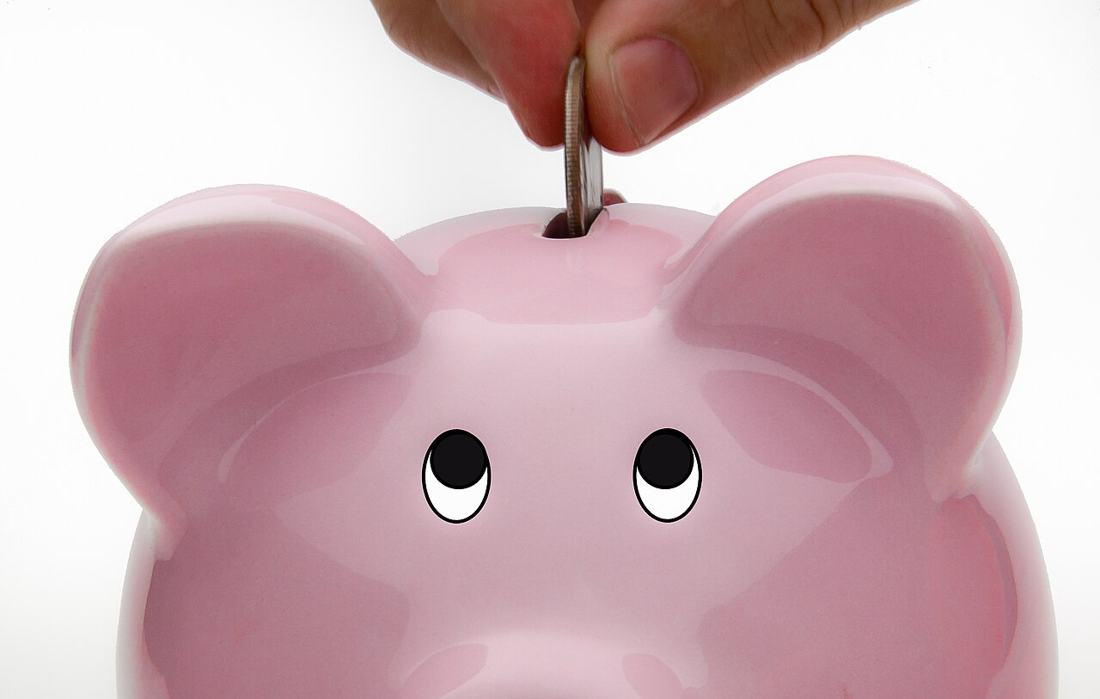 A hand depositing a coin into a piggy bank. Retirement conversion at full retirement age continues your benefit at the same rate. Photo: Wikimedia Commons, CC BY-SA 2.0.